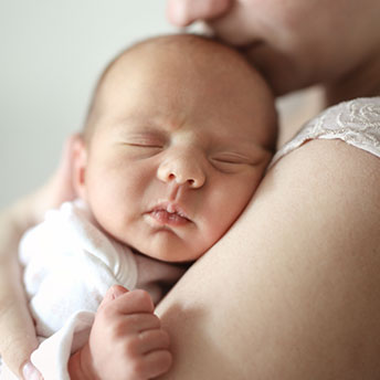 Ein neugeborenes Kind schmiegt sich mit geschlaossenen Augen an die Schulter seiner Mutter.